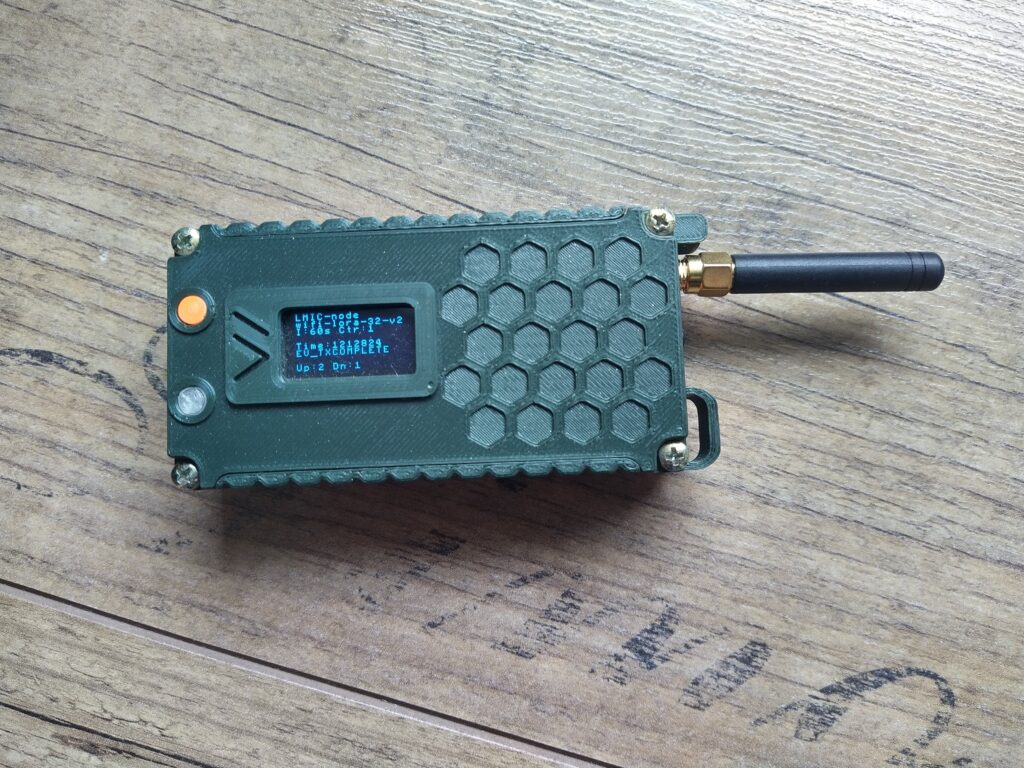 Testovaci zařízení pro sítě The Things Network, krabička podobná starému mobilu s trčící anténkou a textovým displayem.